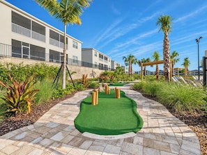 A miniature golf course with a green putting surface, wooden obstacles, and a pathway.
