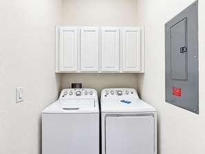A laundry area with two white washing machines, a white wall, and a grey electrical panel.