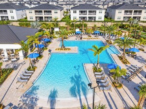 A large swimming pool surrounded by lounge chairs and umbrellas, with a view of residential buildings in the background.