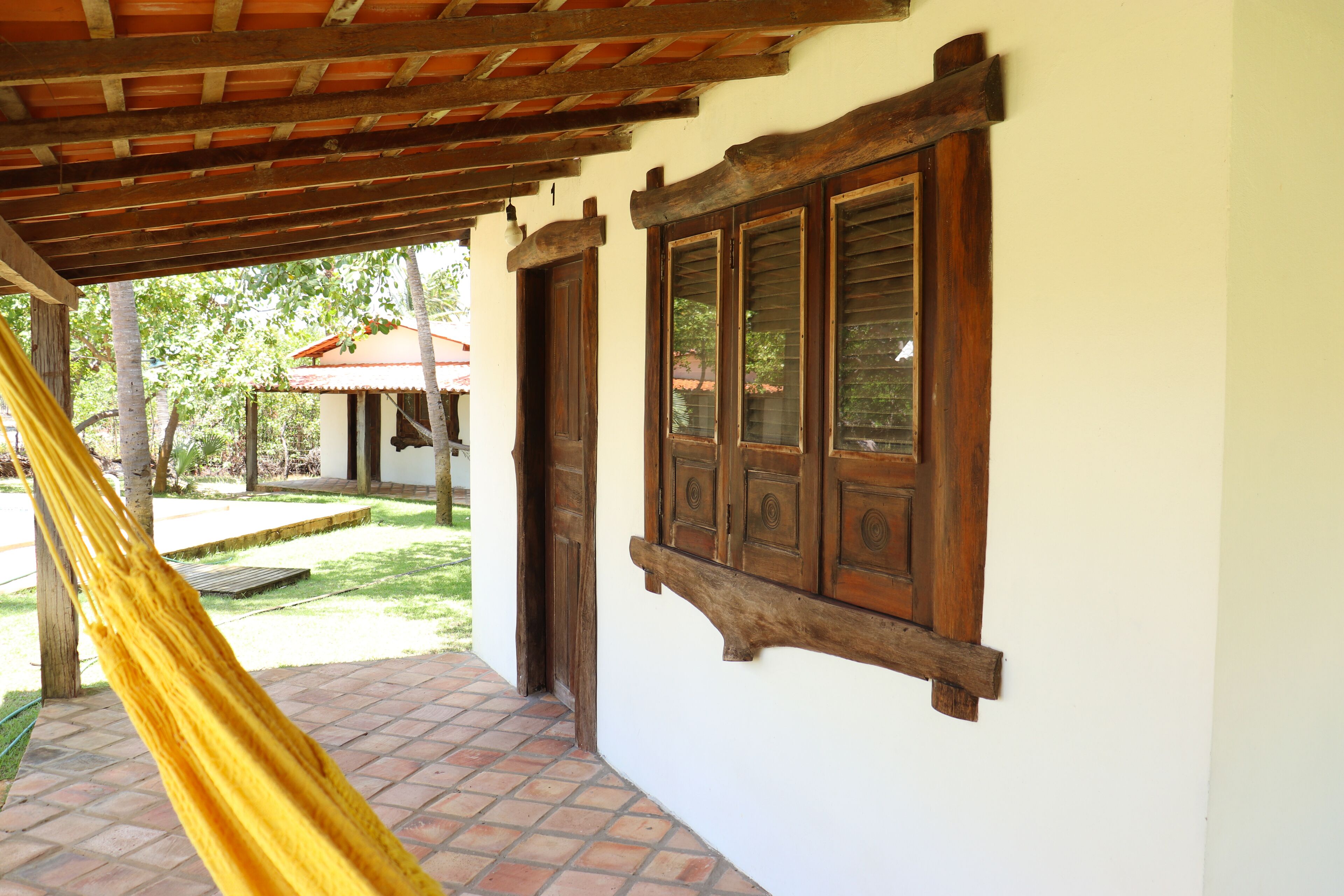 A covered porch with a hammock, wooden window frames, and a tiled floor.