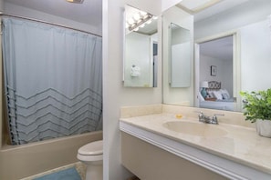 A bathroom with a shower curtain, a toilet, a sink with a mirror, and a potted plant. - Fairway Villa 1304 at Rumbling Bald (Lake Lure)
