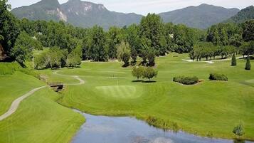 Un campo de golf con un estanque, árboles y montañas al fondo.