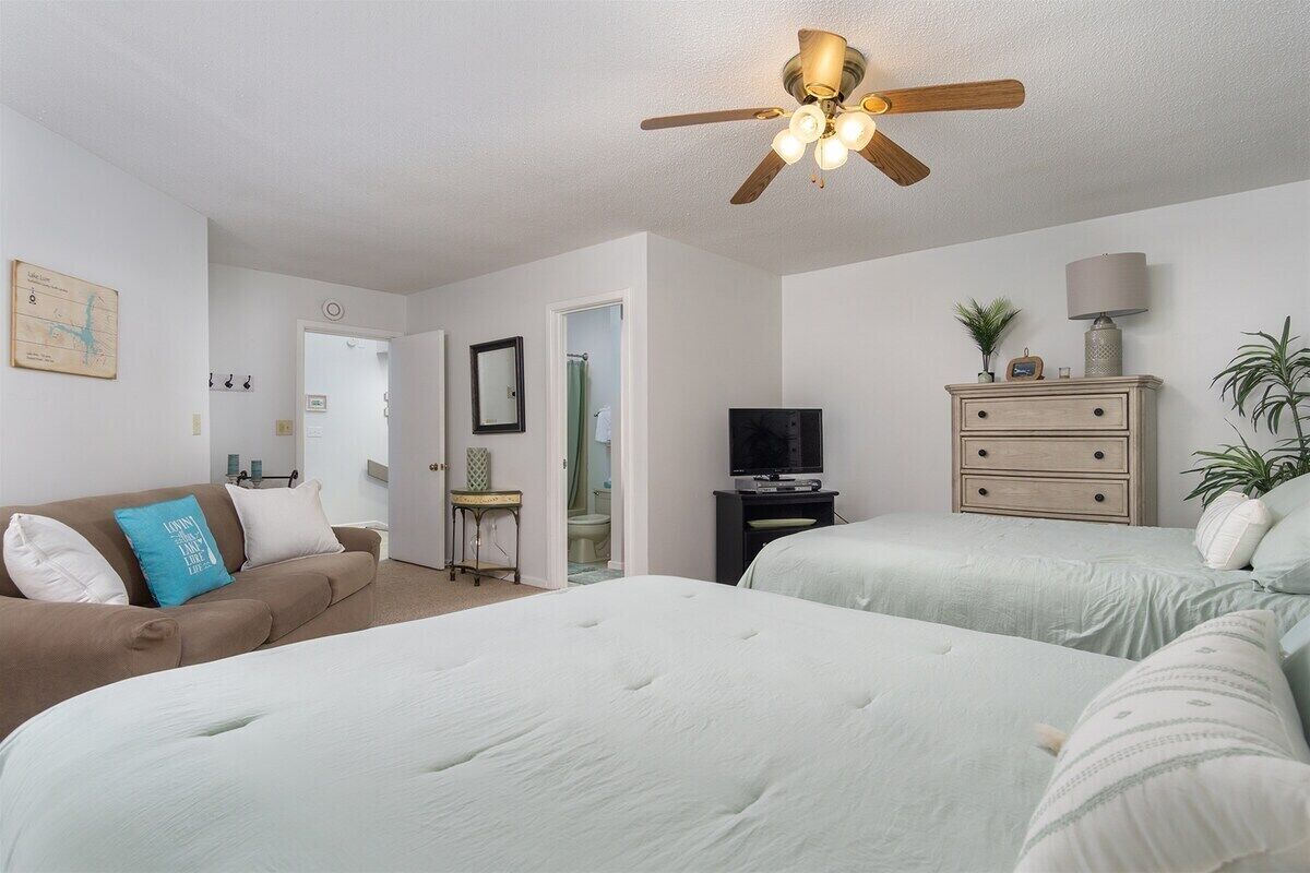 A bedroom with two beds, a ceiling fan, a TV, a dresser, and a small table.
