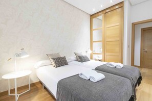 A hotel room with two beds, a nightstand, a lamp, and a wardrobe. - Legazpi | The Rentals Collection (San Sebastián)