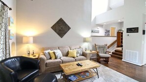 A living room with a sofa, a coffee table, a leather chair, a wooden side table, and a lamp. - Fairway Villa 1403 at Rumbling Bald (Lake Lure)