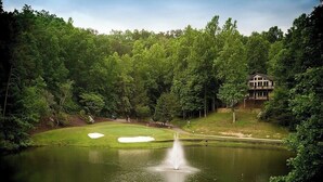 A golf course with a pond, a fountain, and a building in the background. - Fairway Villa 1403 at Rumbling Bald (Lake Lure)