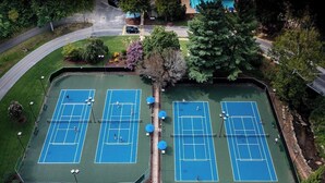 An aerial view of a tennis court complex with multiple courts, surrounded by trees and a road. - Fairway Villa 1403 at Rumbling Bald (Lake Lure)