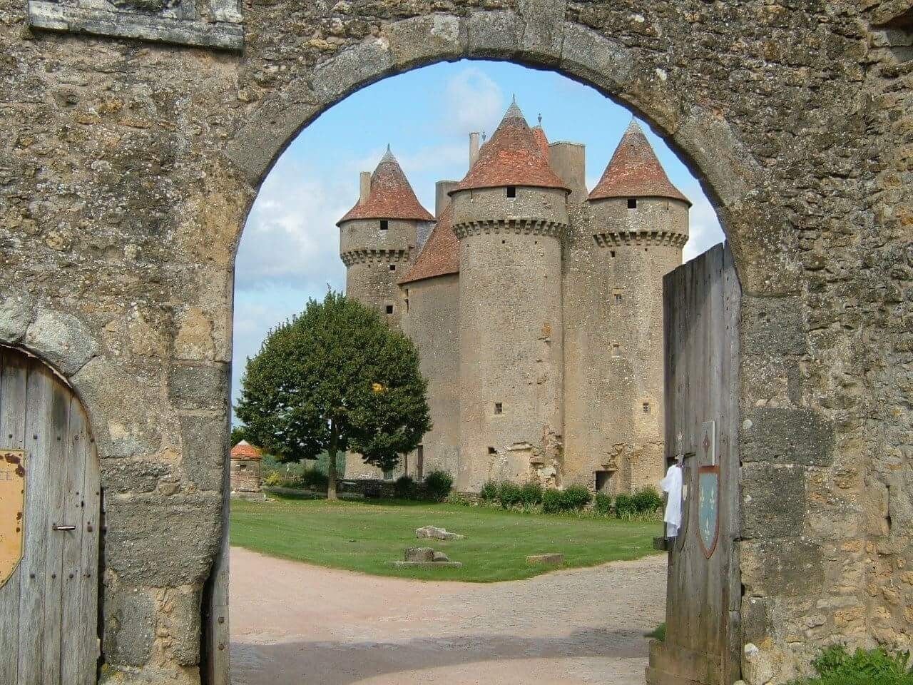 Ein steinernes Tor führt zu einer Burg mit mehreren Türmen und einem grünen Innenhof.
