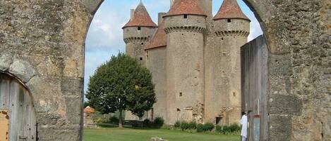 Ein steinernes Tor führt zu einer Burg mit mehreren Türmen und einem grünen Innenhof.