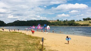A beach with people swimming and playing, a lifeguard tower, and a water slide in the background. - Berrichonne character house (St Jeanvrin)