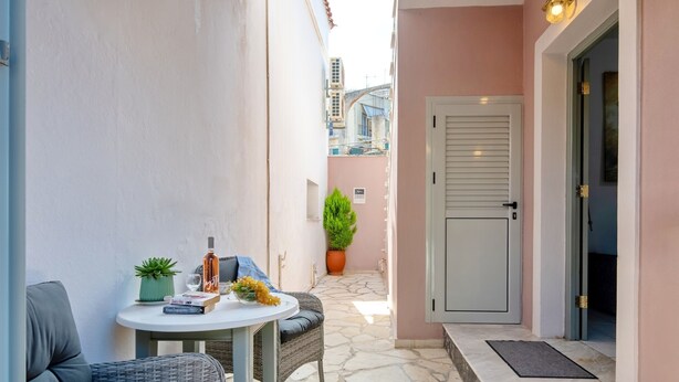 Un étroit couloir extérieur doté d’un sol en pierre, d’une porte blanche et d’une petite table sur laquelle se trouvent une plante et une bouteille.