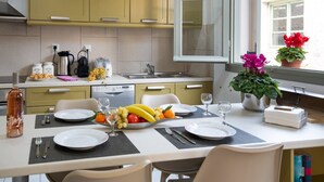 Une cuisine avec des meubles de couleur jaune, une table à manger dressée avec des assiettes, des couverts et un panier de fruits.