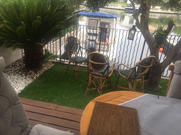 A deck with wicker chairs and a table, overlooking a calm water body and a small dock area with a covered structure.