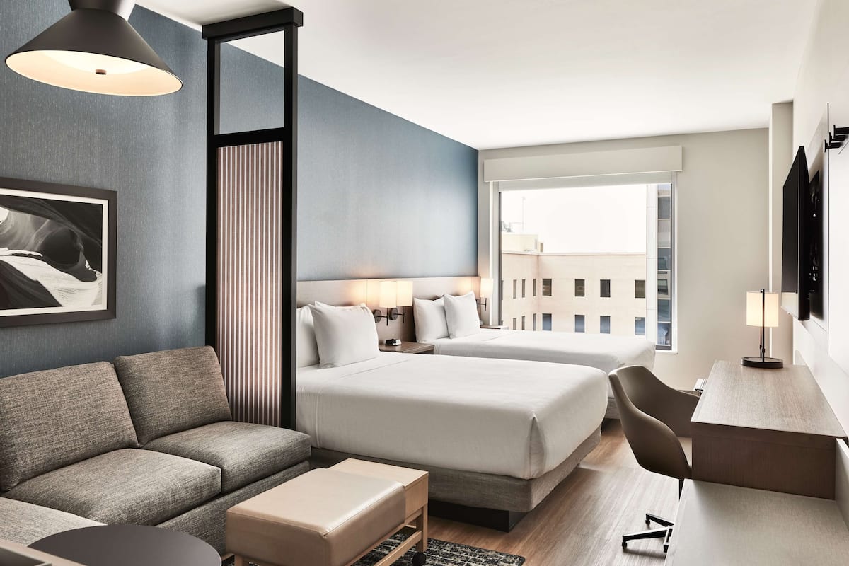A hotel room with two beds, a sofa, a desk, and a TV.