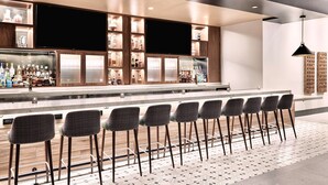 Un espace bar moderne avec un long comptoir, de nombreuses étagères remplies de bouteilles et une rangée de tabourets de bar.
