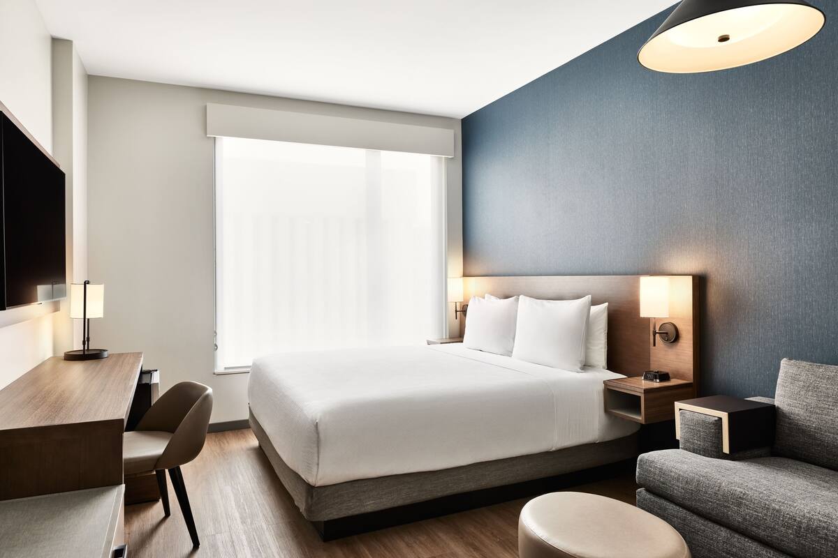 A modern hotel room with a large bed, a desk, a chair, and a sofa.