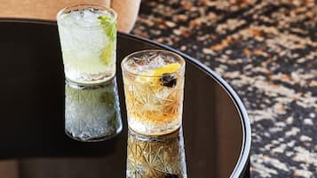 Two glasses of cocktails on a reflective black table with a textured surface.