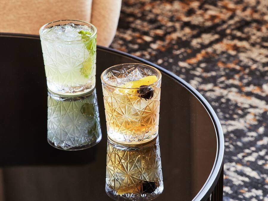 Two glasses of cocktails on a reflective black table with a textured surface.