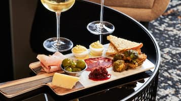 A table with a charcuterie board, including meats, cheeses, olives, and vegetables, accompanied by two glasses of white wine.