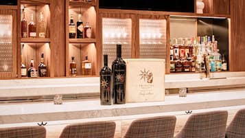 Un espace bar avec des étagères remplies de bouteilles d’alcool, une enseigne « Trinitas Cellars » et des tabourets de bar.