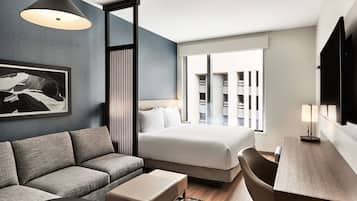 Een moderne hotelkamer met een bank, een bed, een bureau en een groot raam.