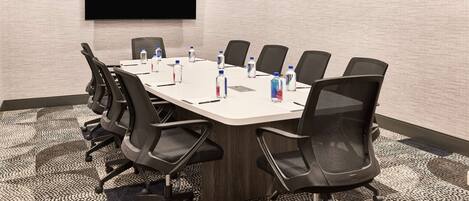 A conference room with a large table, black chairs, a flat-screen TV, and water bottles on the table.