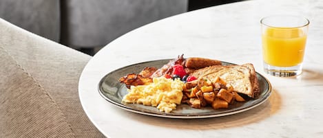 A breakfast plate with scrambled eggs, bacon, toast, and potatoes, accompanied by a glass of orange juice on a round table.