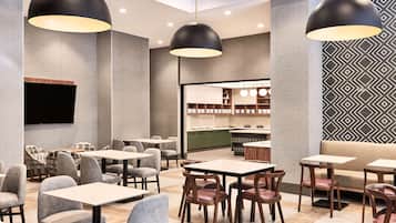 Un restaurante moderno con varias zonas de estar, incluidas mesas y cabinas, y un área de cocina visible al fondo.