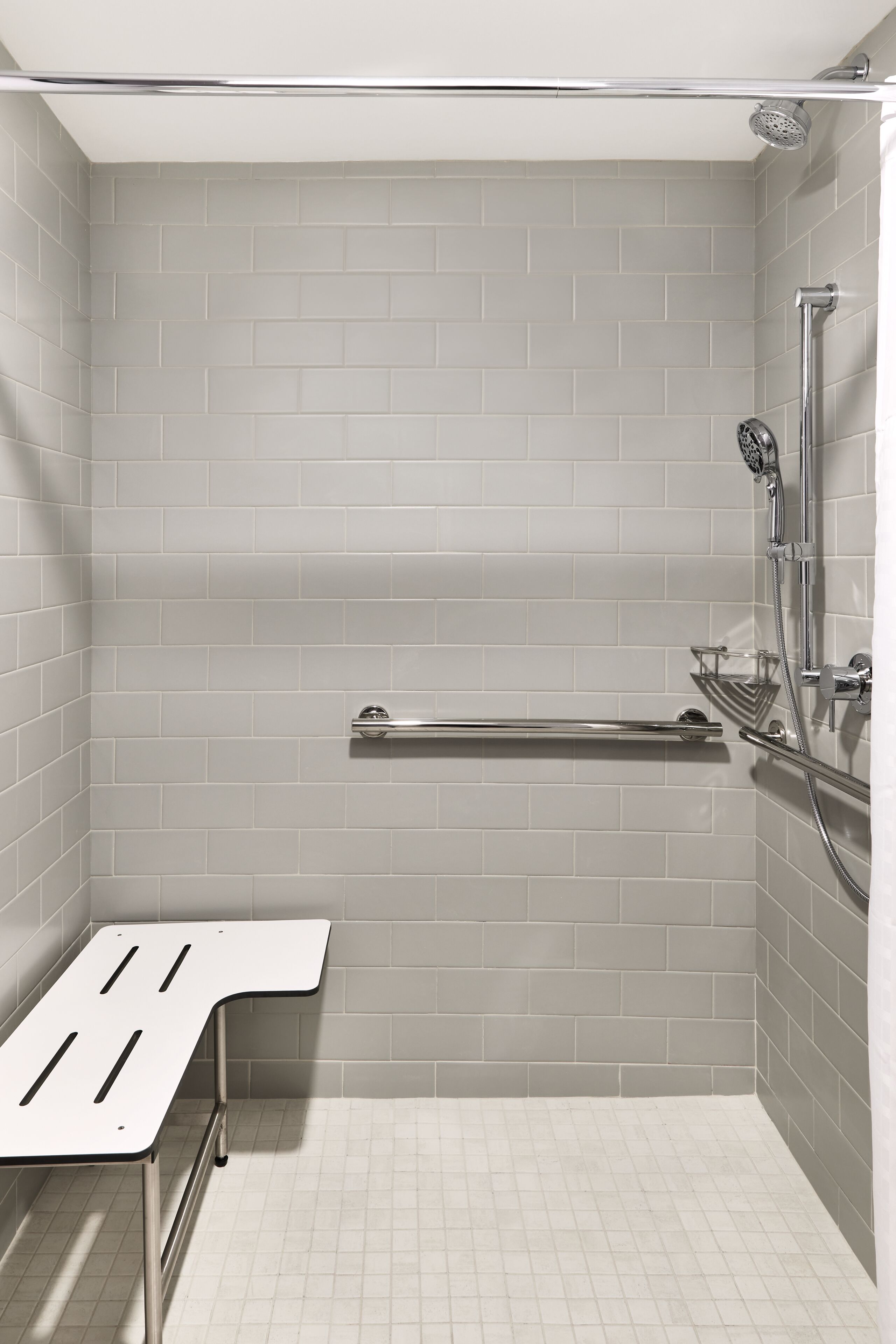 A shower with a handheld showerhead, a handheld shower seat, and a grab bar.