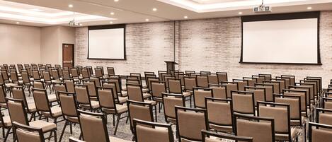 A conference room with rows of chairs, a projector, and a screen.