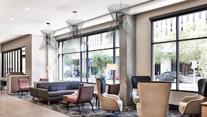 Un hall d’entrée moderne, doté d’un canapé, de fauteuils et d’une table basse. De grandes fenêtres offrent une vue sur la rue.