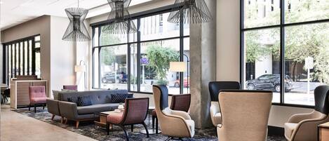 A modern lobby with a sofa, chairs, and a coffee table. Large windows offer a view of the street.