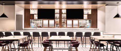 A modern bar area with multiple seating options, a central bar counter, and a view of the city through large windows.