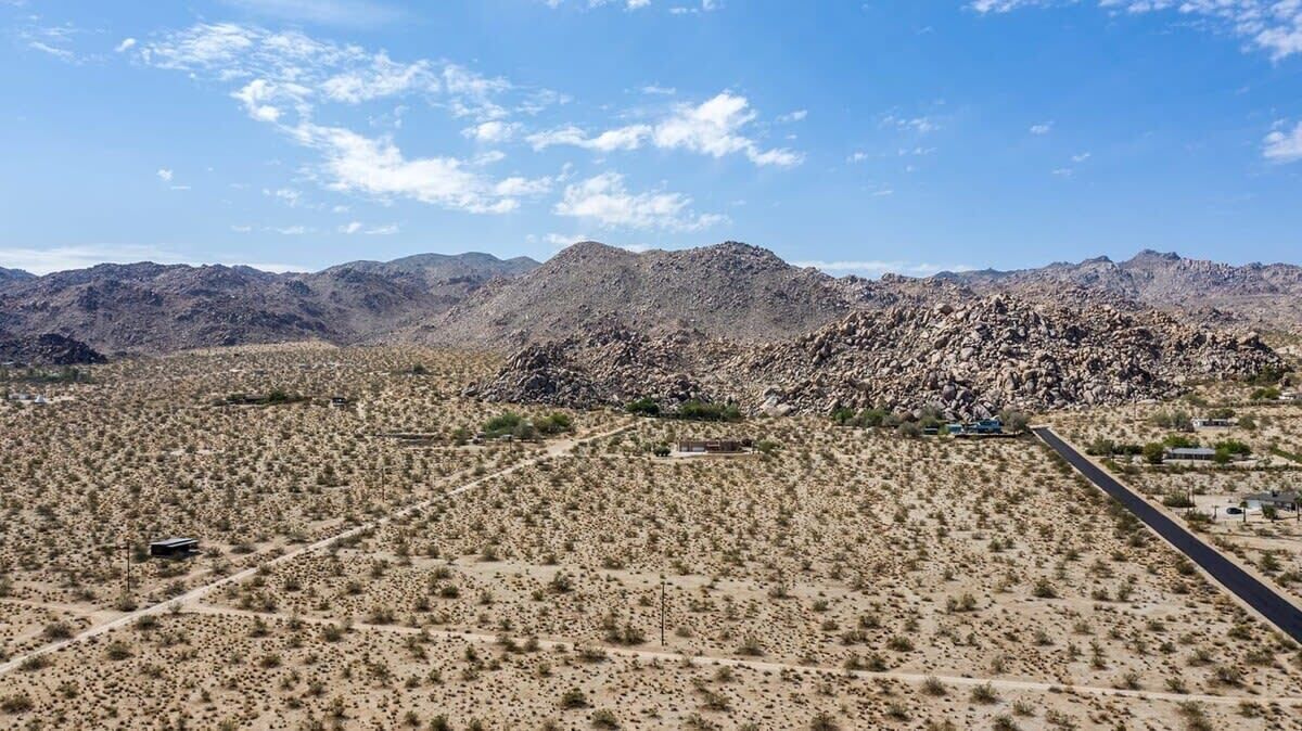 Un paysage désertique avec une végétation clairsemée, une route et des montagnes lointaines sous un ciel dégagé.