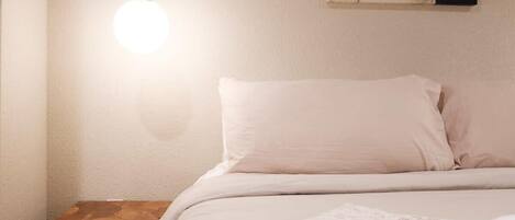 A bedroom with a bed, a bedside table, a hanging light fixture, and a wall-mounted artwork.