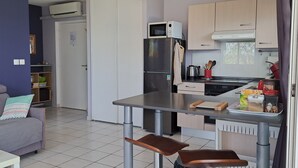 A compact kitchen with a refrigerator, microwave, and stove. There is a dining table with two chairs and a small sofa in the living area.