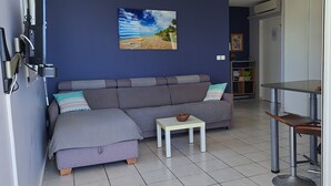 A living room with a grey sofa, a small white table, and a painting of a beach scene on the wall.