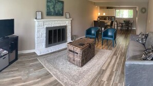 A living room with a fireplace, a television, a sofa, and a dining area with chairs and a table. - Dimmick Cozy Retreat 3 Bed 1 Bath - Sleeps 6 (West Chester Township)