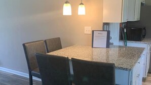 A modern kitchen with a granite countertop, dark chairs, and pendant lighting. - Dimmick Cozy Retreat 3 Bed 1 Bath - Sleeps 6 (West Chester Township)