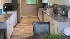 A modern kitchen with granite countertops, white cabinets, and a dining area with a round table and chairs. - Dimmick Cozy Retreat 3 Bed 1 Bath - Sleeps 6 (West Chester Township)
