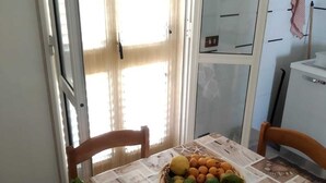 A dining table with a patterned tablecloth, a basket of fruits, and a bowl of greens.