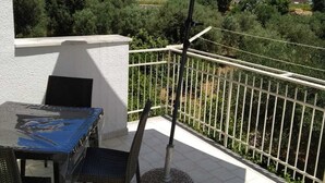 A patio with a table and chairs, an umbrella, and a view of greenery and buildings in the background.