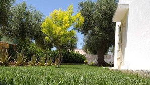 A well-maintained lawn with a variety of trees and shrubs, a white building with a visible door, and a clear blue sky.
