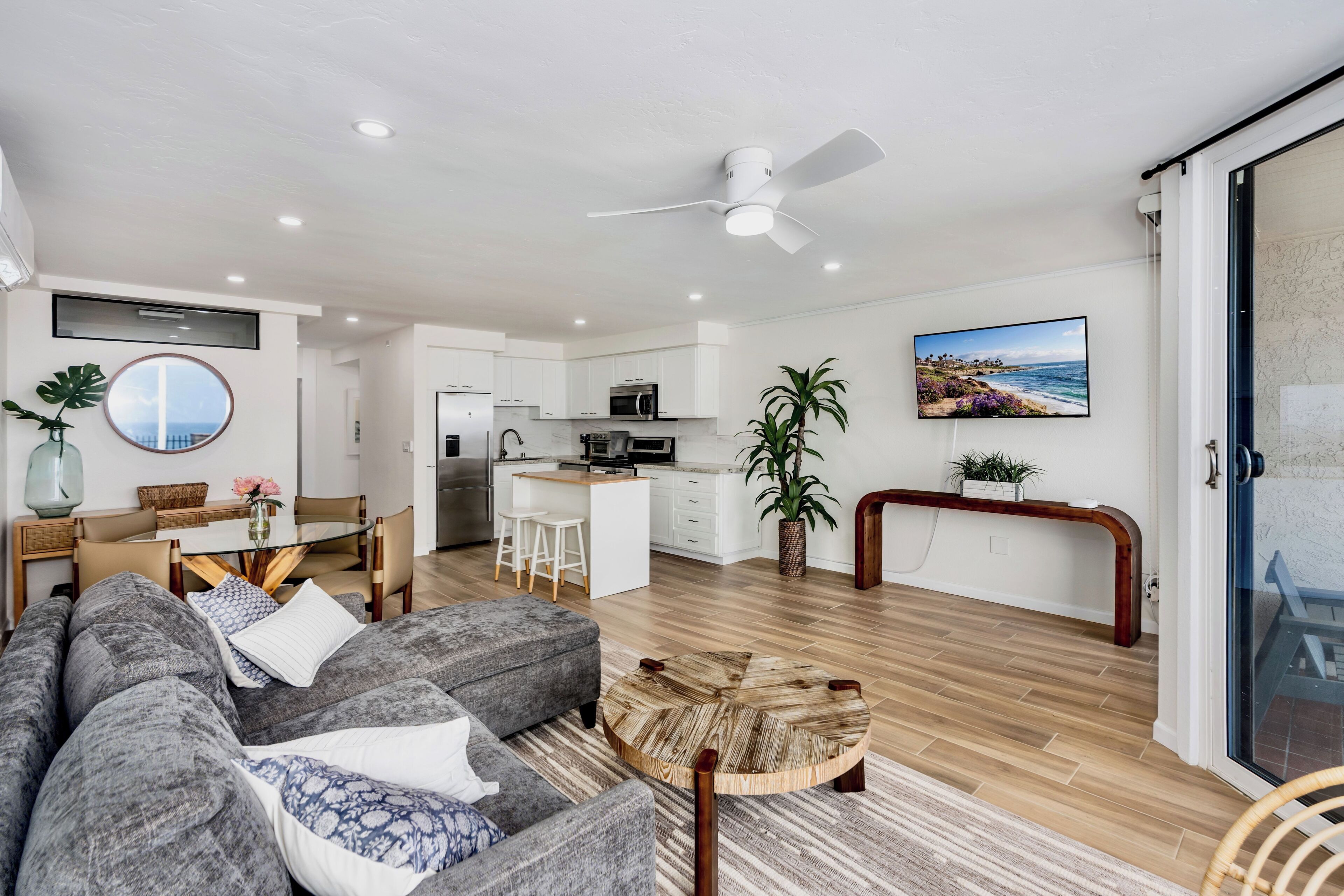 A modern living space with a grey sofa, a dining area, a kitchen, and a view of the ocean.