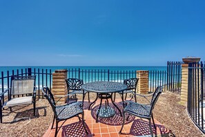 Zona d'estar a l'exterior amb taula i caires, vista a l'oceà i una tanca metàl·lica.