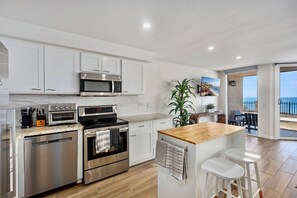 A modern kitchen with stainless steel appliances, a wooden island, and a view of the sea through an open door. - Oceanfront | Hot Tub | Heated Pool | Beach Access (Solana Beach)