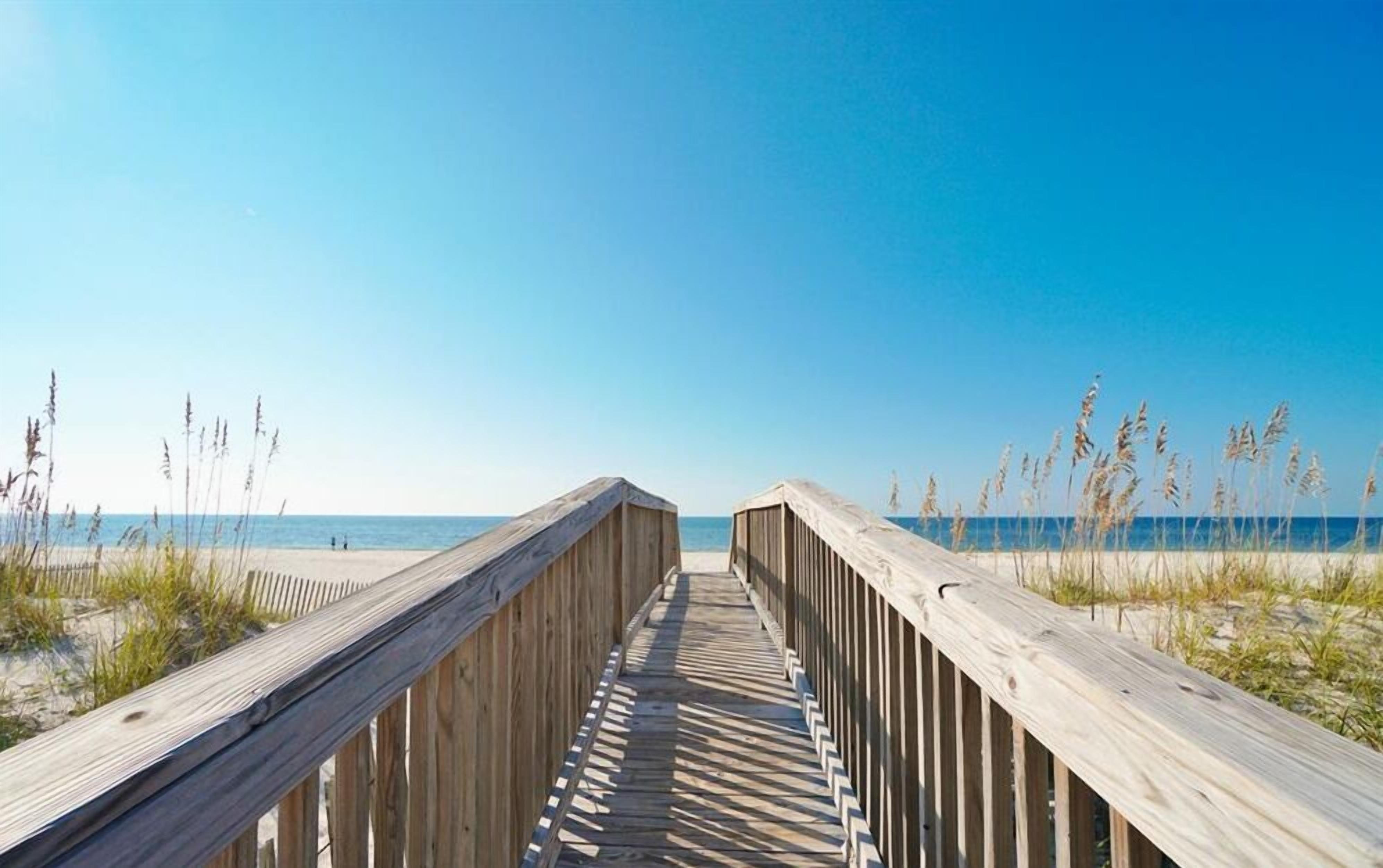 A wooden boardwalk leading to a beach with clear skies.
