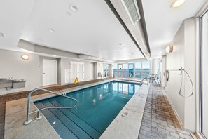 Una piscina coberta moderna amb parets de vidre transparent, un solàrium amb rajoles i vista cap a l'exterior.