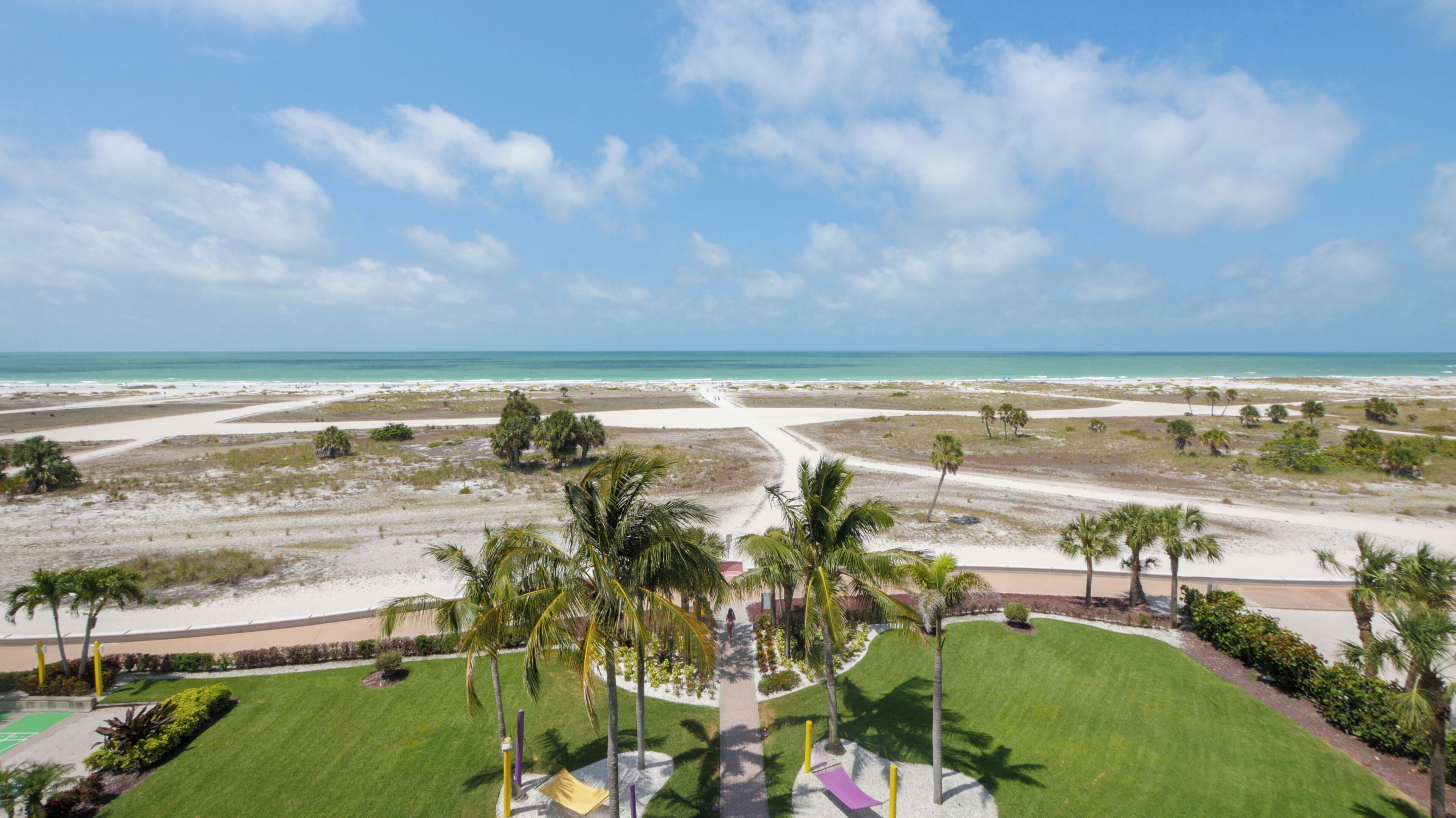 A coastal landscape with a beach, palm trees, and a clear sky.