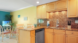 Una cocina con armarios de madera, encimera de granito, lavavajillas y un comedor con sillas y una mesa.